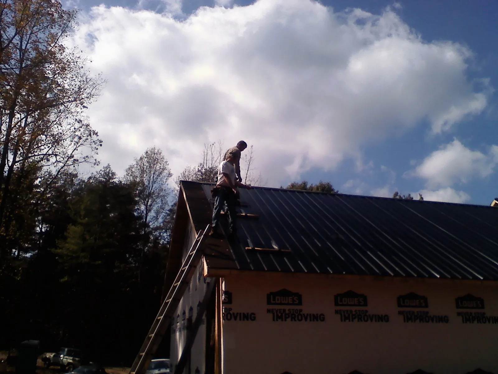 Roofer fastening dark metal panels high against a cloudy sky in Denton